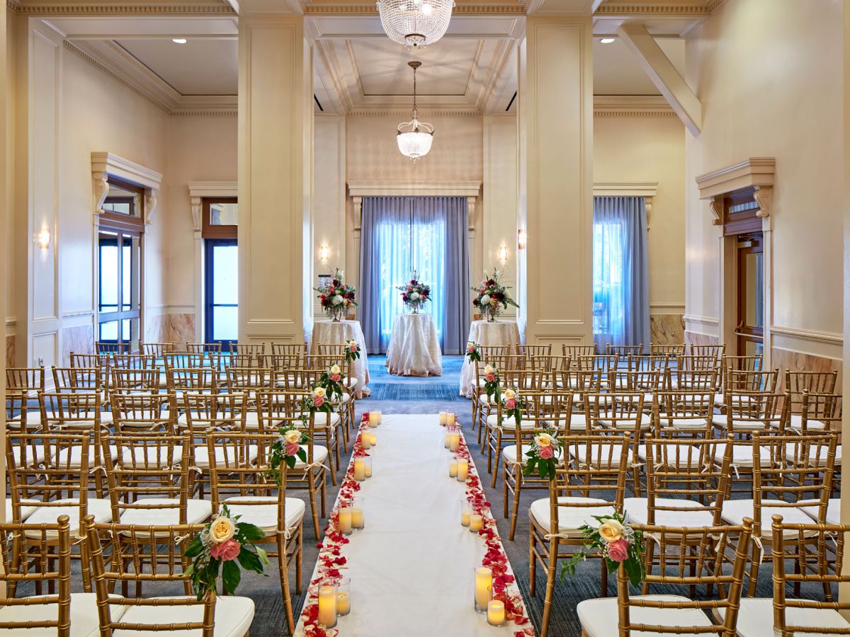 An elegant wedding setup with golden chairs, floral centerpieces, and a candle-lit aisle leading to a decorated stage.